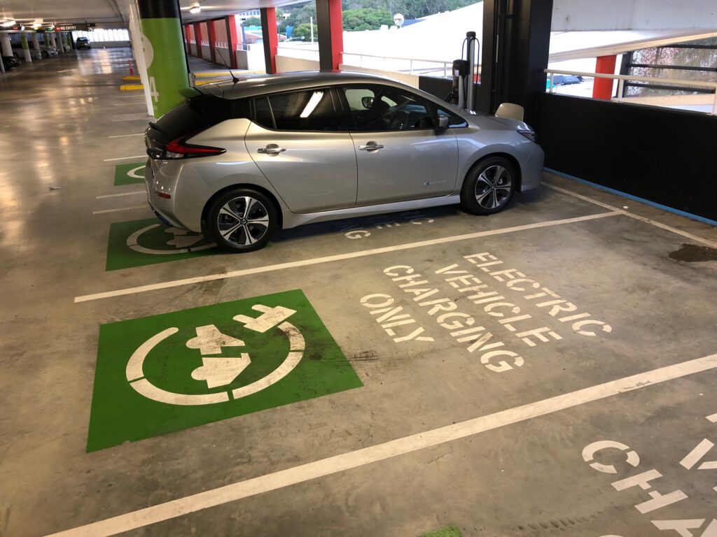 Nissan Leaf being charged at a public charging station in a shopping centre carpark